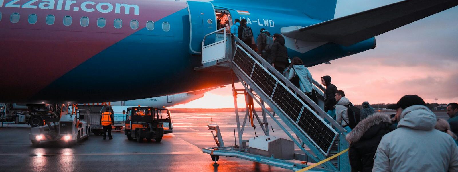 Passengers boarding an airplane at sunset with a vivid sky in the background, capturing a travel moment.