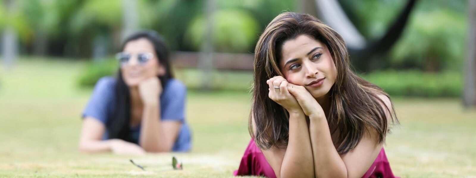 Young women enjoying a sunny day at a park in Bengaluru, India, lying on the grass and posing naturally.