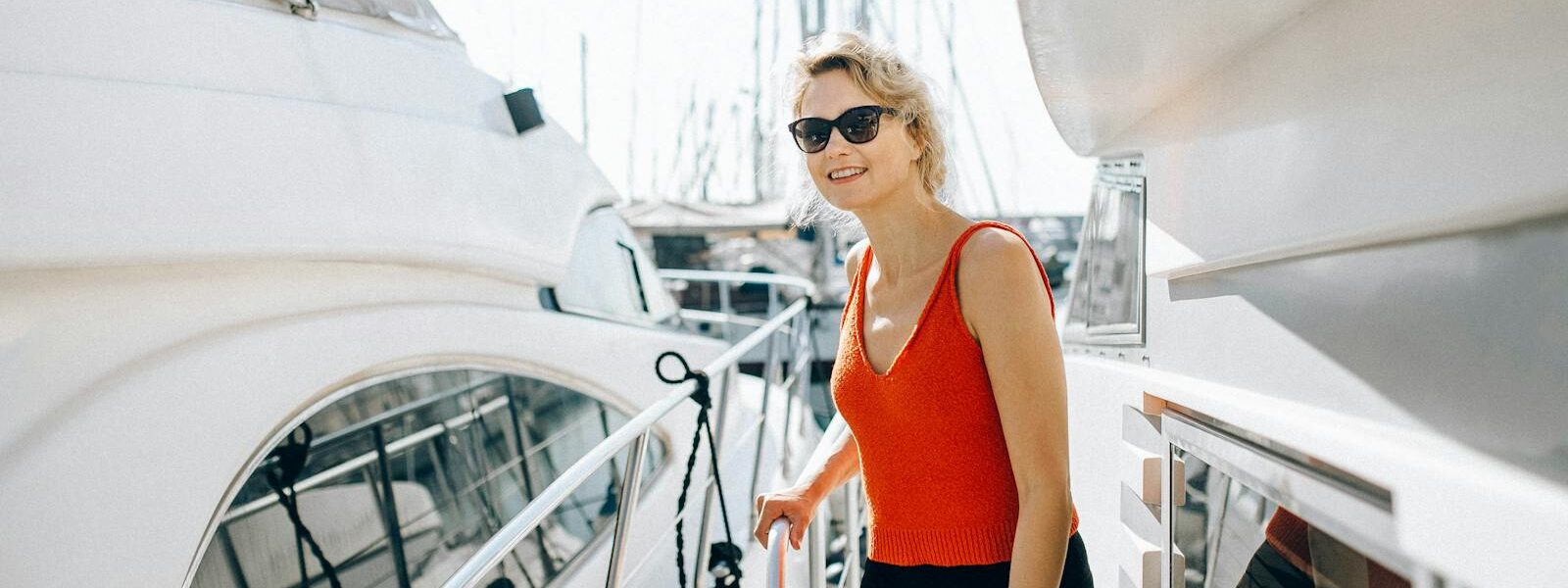A woman in sunglasses stands on a yacht, enjoying a sunny day outdoors.