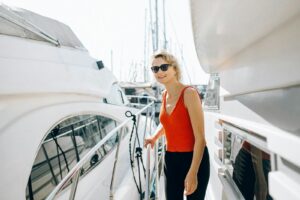 A woman in sunglasses stands on a yacht, enjoying a sunny day outdoors.